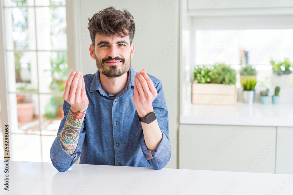 Young man wearing casual shirt sitting on white table Doing money gesture with hand, asking for salary payment, millionaire business Young man wearing casual shirt sitting on white table Doing money gesture with hand, asking for salary payment, millionaire business