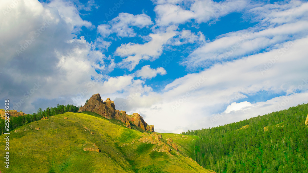 Summer landscape high hill with large stones and blue sky with air clouds. Russia Siberia.