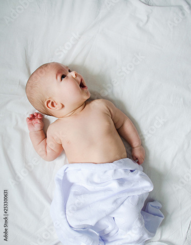 naked baby is smiling in a white bed photo