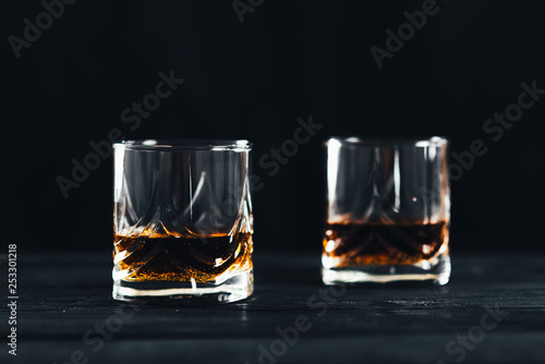 Two glasses with ice and whiskey on wooden background