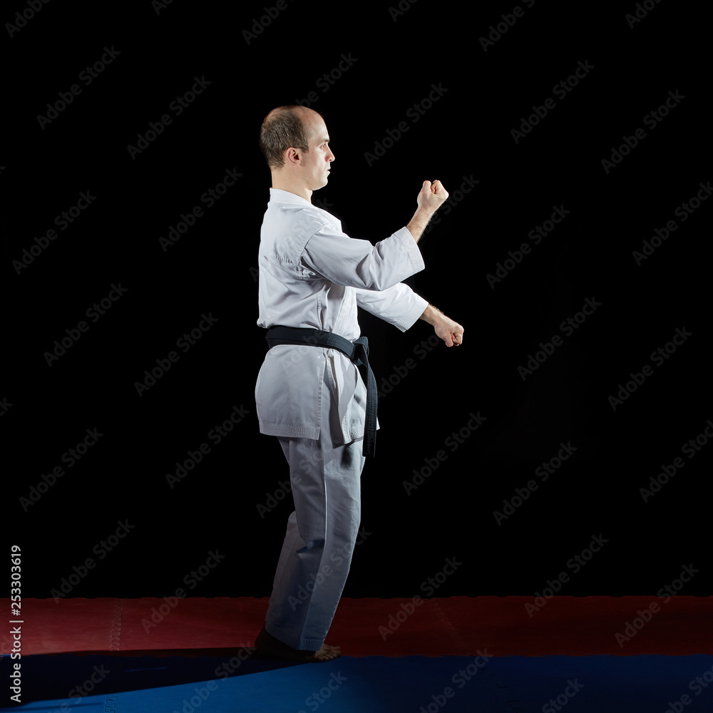 Adult athlete trains formal karate exercises on red and blue tatami