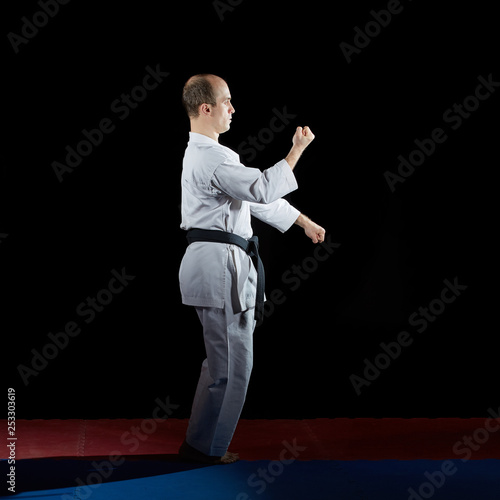 Adult athlete trains formal karate exercises on red and blue tatami