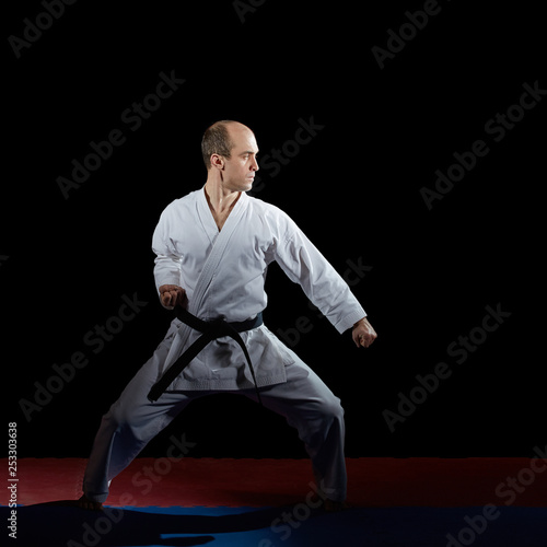 Active athlete does formal karate exercises on red and blue tatami