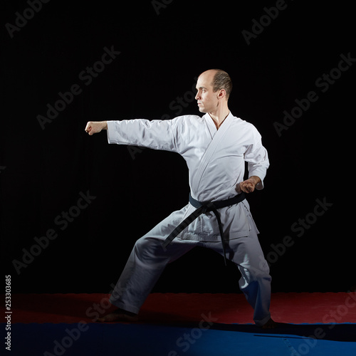 Adult athlete doing formal karate exercises on red and blue tatami