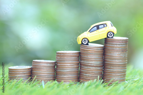 Miniature yellow car model on growing stack of coins money on nature green background, Saving money for car, Finance and car loan, Investment and business concept photo