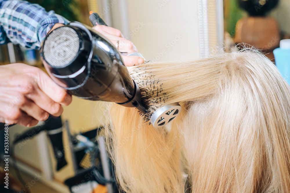 Professional hairdresser makes head design, dries hair with a hair dryer and combs with a round brush. Beauty shop. Female beauty. Professional hairdresser makes head design, dries hair with a hair dryer and combs with a round brush. Beauty shop. Female beauty.