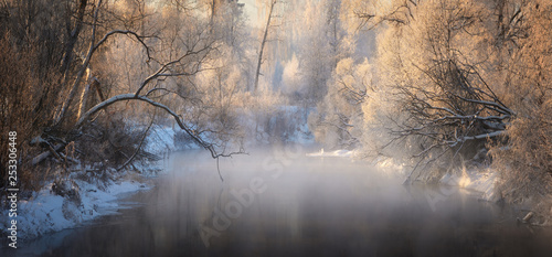 Winter landscape with river, snow-covered trees, fog and hoarfrost. Winter sunrise on river with fog.