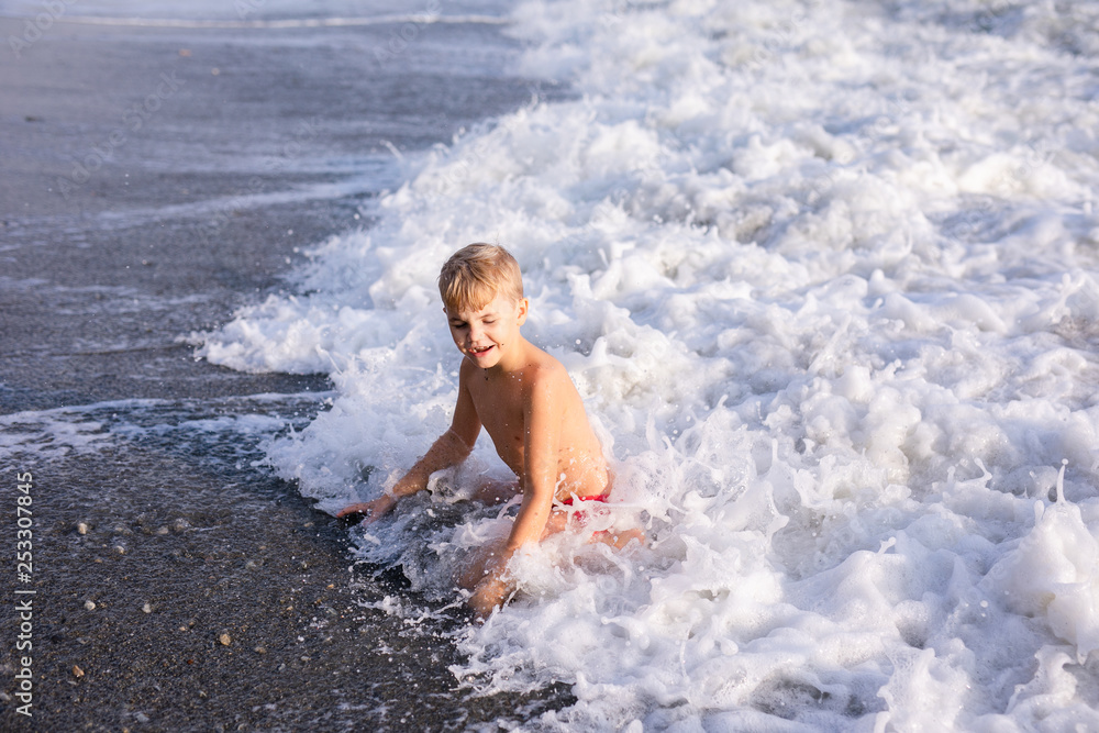 Boy jumping in sea waves. Jump accompanied by water splashes. Summer sunny day, ocean coast