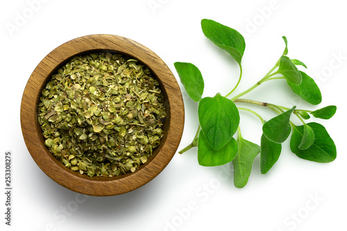 Dried chopped oregano in dark wood bowl next to fresh oregano leaves isolated on white from above.