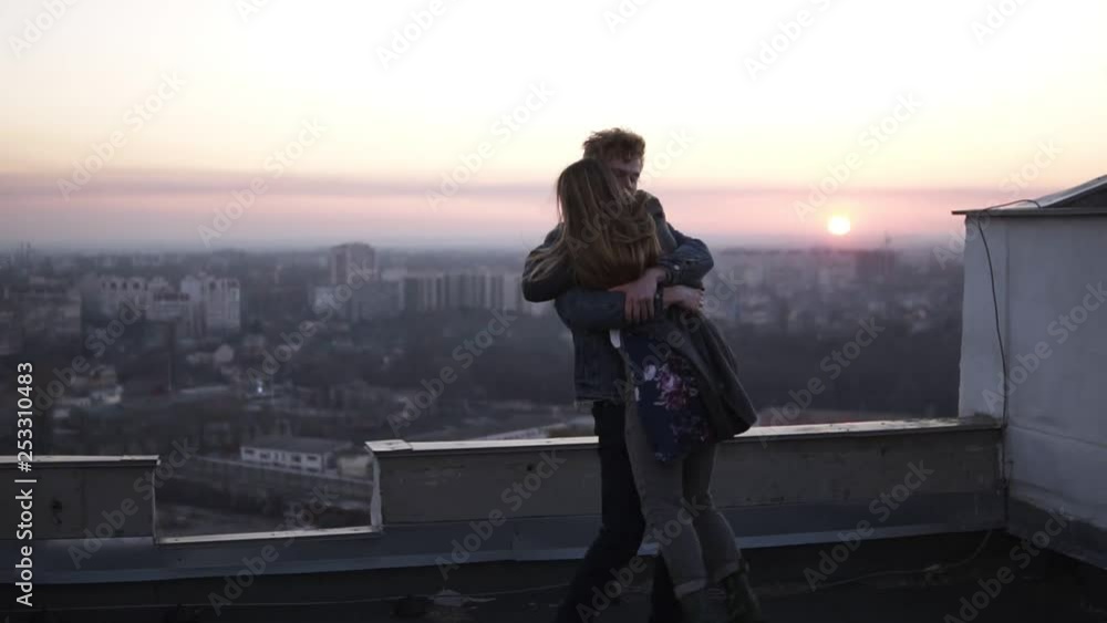 Redhead guy whirls his girlfriend on the roof with a cityscape and sunset horizon on the background. Happy time together, dating in romantic places Redhead guy whirls his girlfriend on the roof with a cityscape and sunset horizon on the background. Happy time together, dating in romantic places