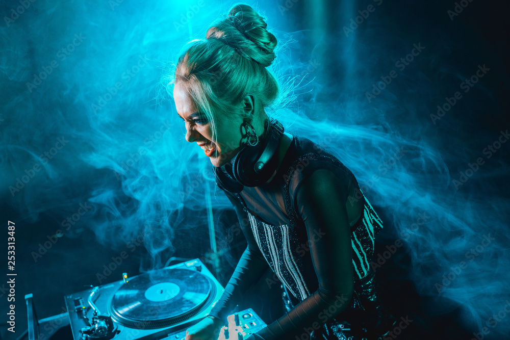 Obraz premium angry blonde dj girl using dj equipment in nightclub with smoke