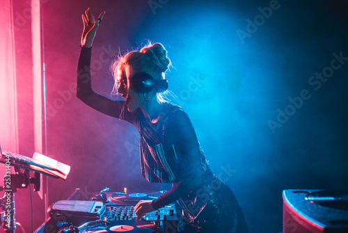 happy dj girl with blonde hair using dj mixer in nightclub with smoke photo