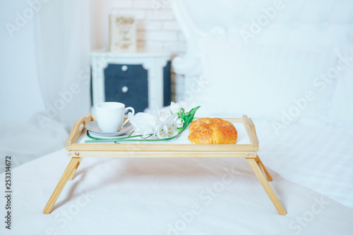 Breakfast tray in bed: white cup, croissants and flowers