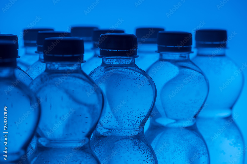 close up of plastic water bottles in rows on neon blue background close up of plastic water bottles in rows on neon blue background