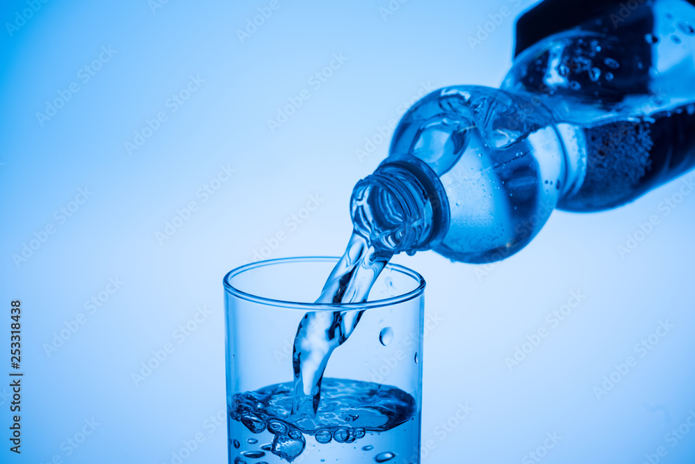 water pouring from plastic bottle in glass on blue background with copy space water pouring from plastic bottle in glass on blue background with copy space