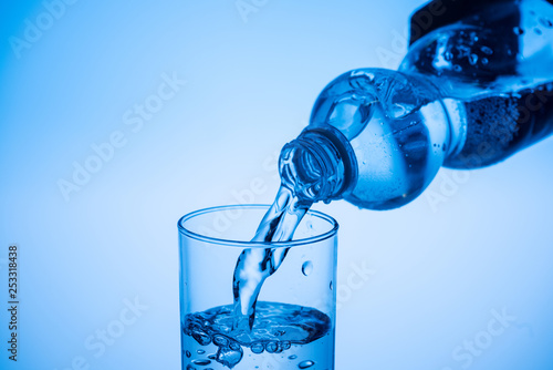water pouring from plastic bottle in glass on blue background with copy space