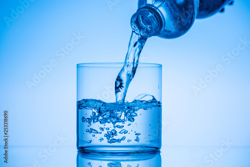 water pouring from plastic bottle in drinking glass on blue background