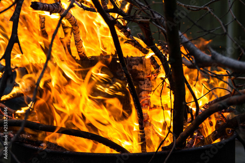 Branches and twigs being burnt in a garden incinerator. Sparks, flames are visible.