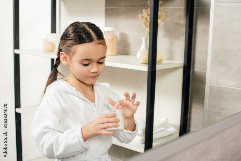 selective focus of child in white bathrobe with cosmetic cream in bathroom