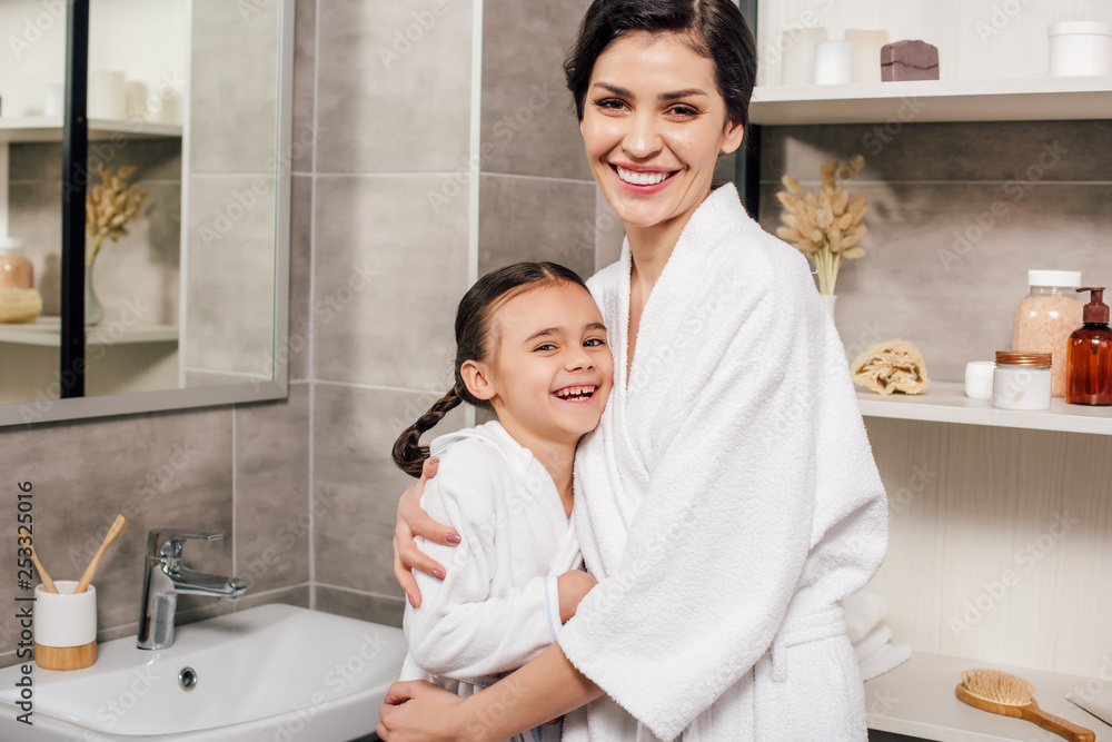 daughter and mother in white bathrobes hugging and smiling in bathroom daughter and mother in white bathrobes hugging and smiling in bathroom