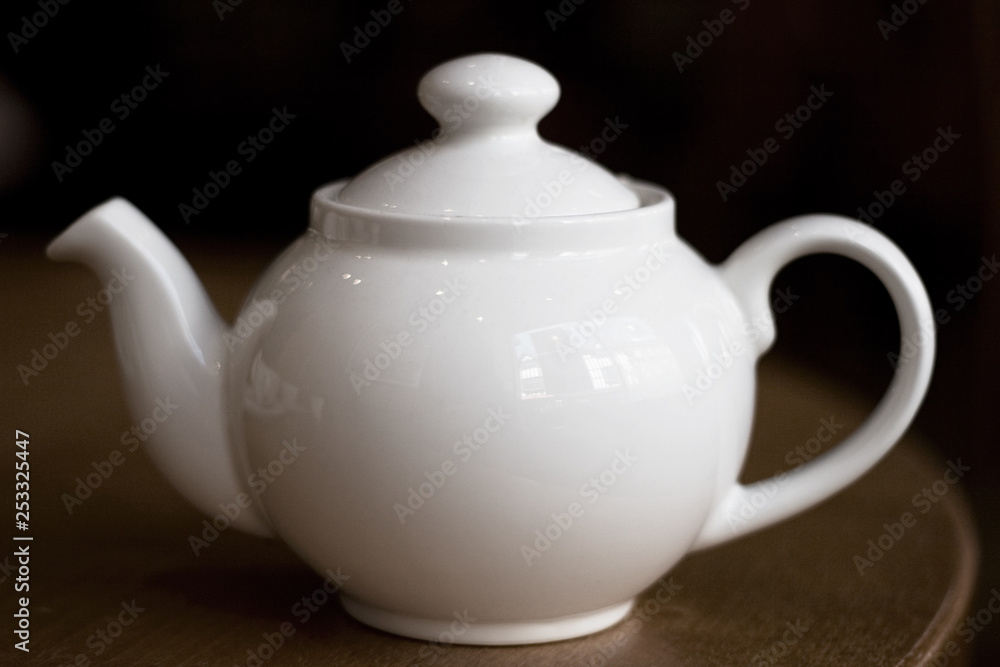 White teapot on a dark wood table with dark background. Tea drinking, coffee drinking, britishness, coffee culture concepts. White teapot on a dark wood table with dark background. Tea drinking, coffee drinking, britishness, coffee culture concepts.