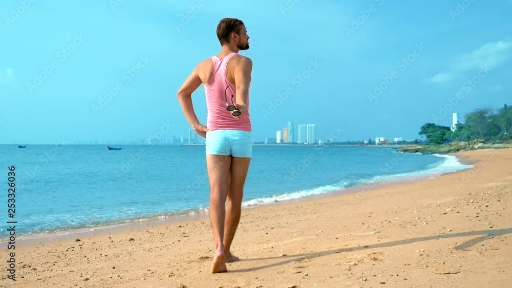 Playful handsome guy in a pink t-shirt and blue shorts rejoices at the beach. freak on the sea. Playful handsome guy in a pink t-shirt and blue shorts rejoices at the beach. freak on the sea.