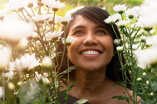 Young tanned asian girl smiling in a wild flower field with the sun on her face