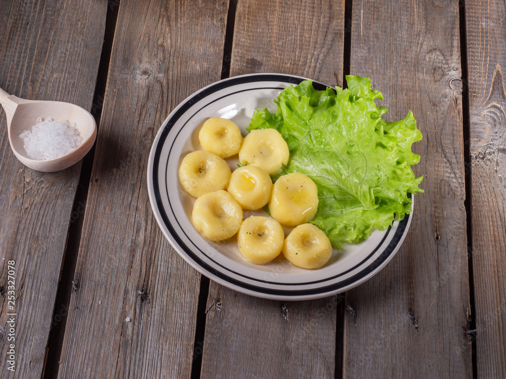 Cooked potato gnocchi, leaves of fresh leaf lettuce on a striped bright ceramic plate on an old plank table. Cooked potato gnocchi, leaves of fresh leaf lettuce on a striped bright ceramic plate on an old plank table.