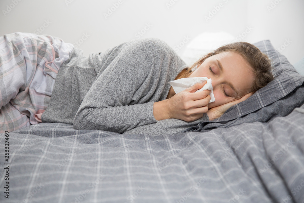 Sick woman lying in bed with closed eyes, blowing nose Sick woman lying in bed with closed eyes, blowing nose