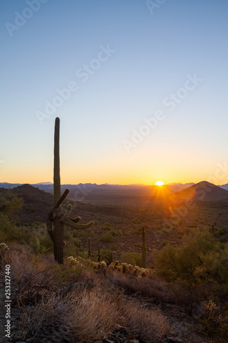 The sun rising above the Arizona Desert with the Four Peaks in the distant background and a clear blue sky.