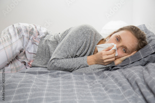 Sick woman lying in bed, looking at camera, blowing nose 