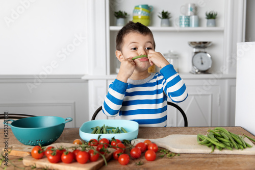 Boy making mustache with green bean at home photo