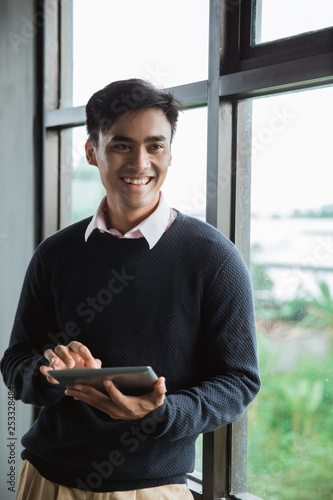 a businessman holding digital tablet look at the camera in front the windows in the office room