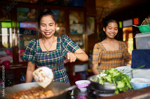 thai mother and daughter cooking together in rustic kitchen making red curry