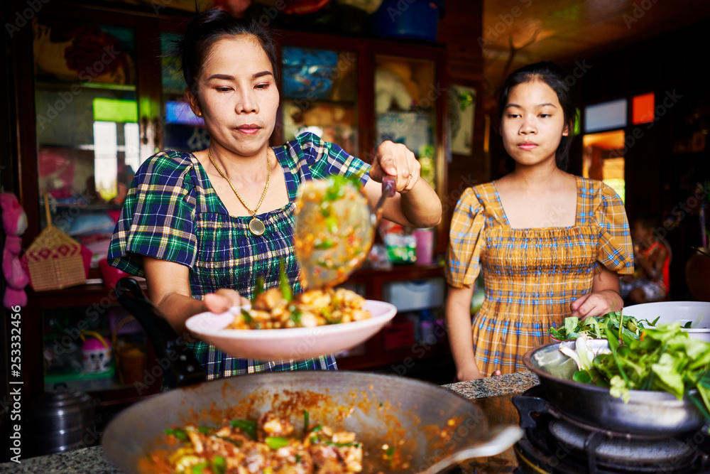 thai mother and daughter plating freshly cooked red curry in rustic traditional kitchen