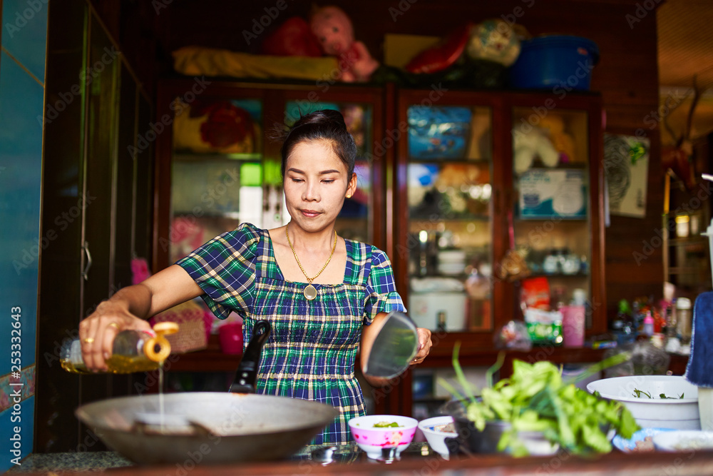 thai woman pouring oil in wok in traditional home kitchen