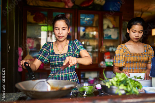 thai mother and daughter cooking red curry together in rustic kitchen