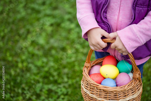 Little girl hunts Easter egg. Kids searching eggs in the garden. Child holds a basket with colored eggs.
