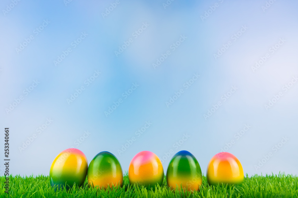 Colorful Easter eggs in a row in the grass, blue sky background