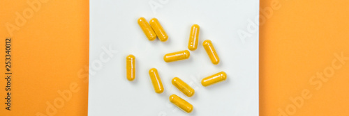 Yellow vitamin pills on orange background, banner