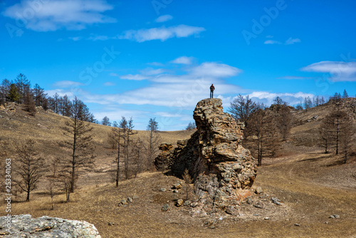 Wide steppe with yellow grass under a blue sky with white clouds and men silhouette on top of hill, Tazheran steppe, Siberia Russia photo