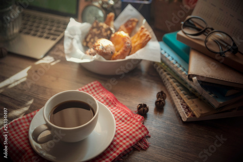 Cup of Coffee with bread (breakfast),Desktop laptop,headphone,clock and diary,books and glasses on blue wooden desk,Working space at home.Urban Lifestyle concept