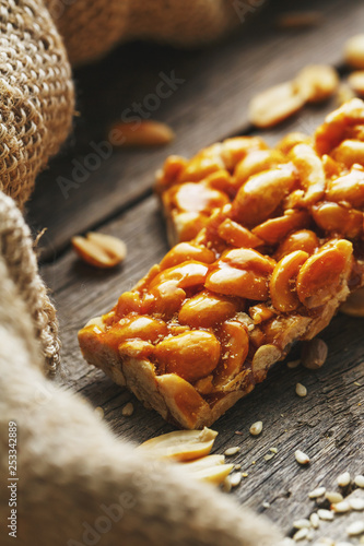 Sweets bar of peanuts on a vintage background with burlap. Delicious oriental sweets Gozinaki from sunflower seeds, sesame and peanuts, covered with honey with a shiny icing