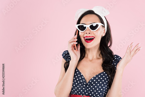 Attractive brunette woman in sunglasses talking on smartphone isolated on pink