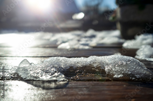 Melting snow on a wooden table in the warm, bright rays of the spring sun, on a blurred background. © koldunova