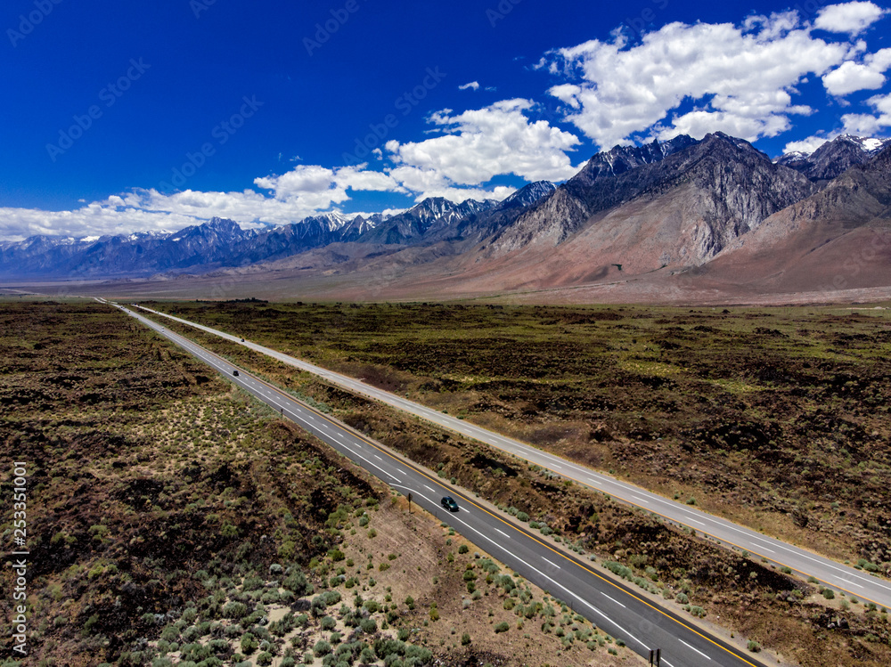 Fototapeta premium Aerial, drone view of Owens Valley and the snowcapped Eastern Sierra Nevada Mountains along California State Highway 395 in the spring with blue sky, white clouds, purple mountains and green flora