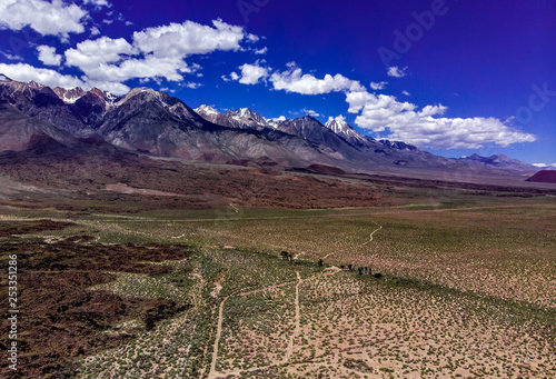 Aerial  drone view of Owens Valley and the snowcapped Eastern Sierra Nevada Mountains along California State Highway 395 in the spring with blue sky  white clouds  purple mountains and green flora
