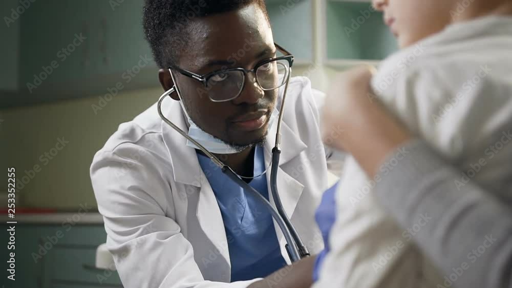 Young african pediatrician examining little male patient using stethoscope in the hospital office. Young african pediatrician examining little male patient using stethoscope in the hospital office.