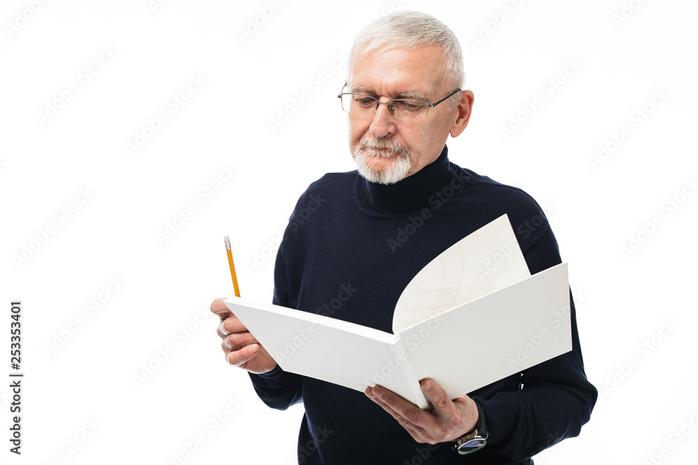 Old handsome man with gray hair and beard in eyeglasses and sweater thoughtfully reading book holding pencil in hand over white background isolated Old handsome man with gray hair and beard in eyeglasses and sweater thoughtfully reading book holding pencil in hand over white background isolated