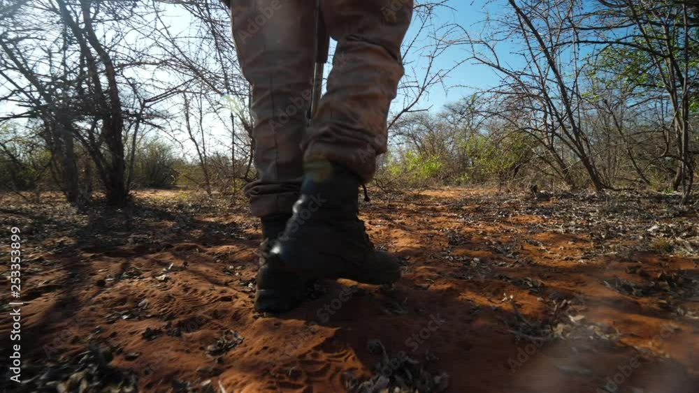 Medium, low following shot of African ranger's boots as he is tracking through bushes in sandy area Medium, low following shot of African ranger's boots as he is tracking through bushes in sandy area
